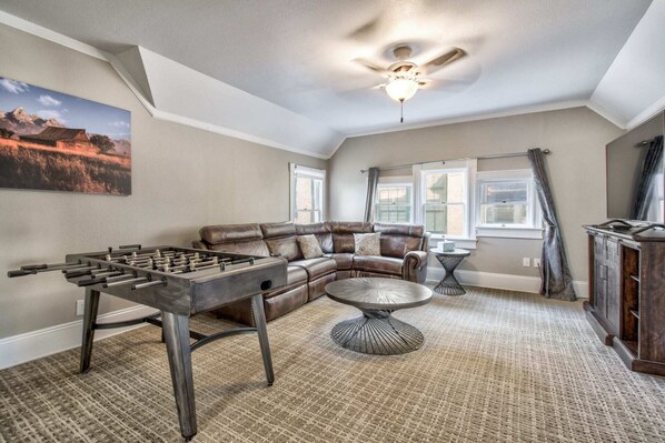 A living room with a foosball table, a leather sofa, a coffee table, and a ceiling fan.