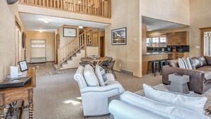 A spacious living area with a high ceiling, a staircase, a kitchen, and a mounted animal head.