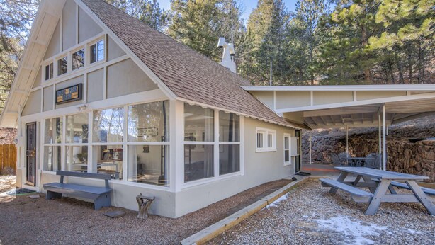 A cabin with large windows, a covered patio, and a stone wall.