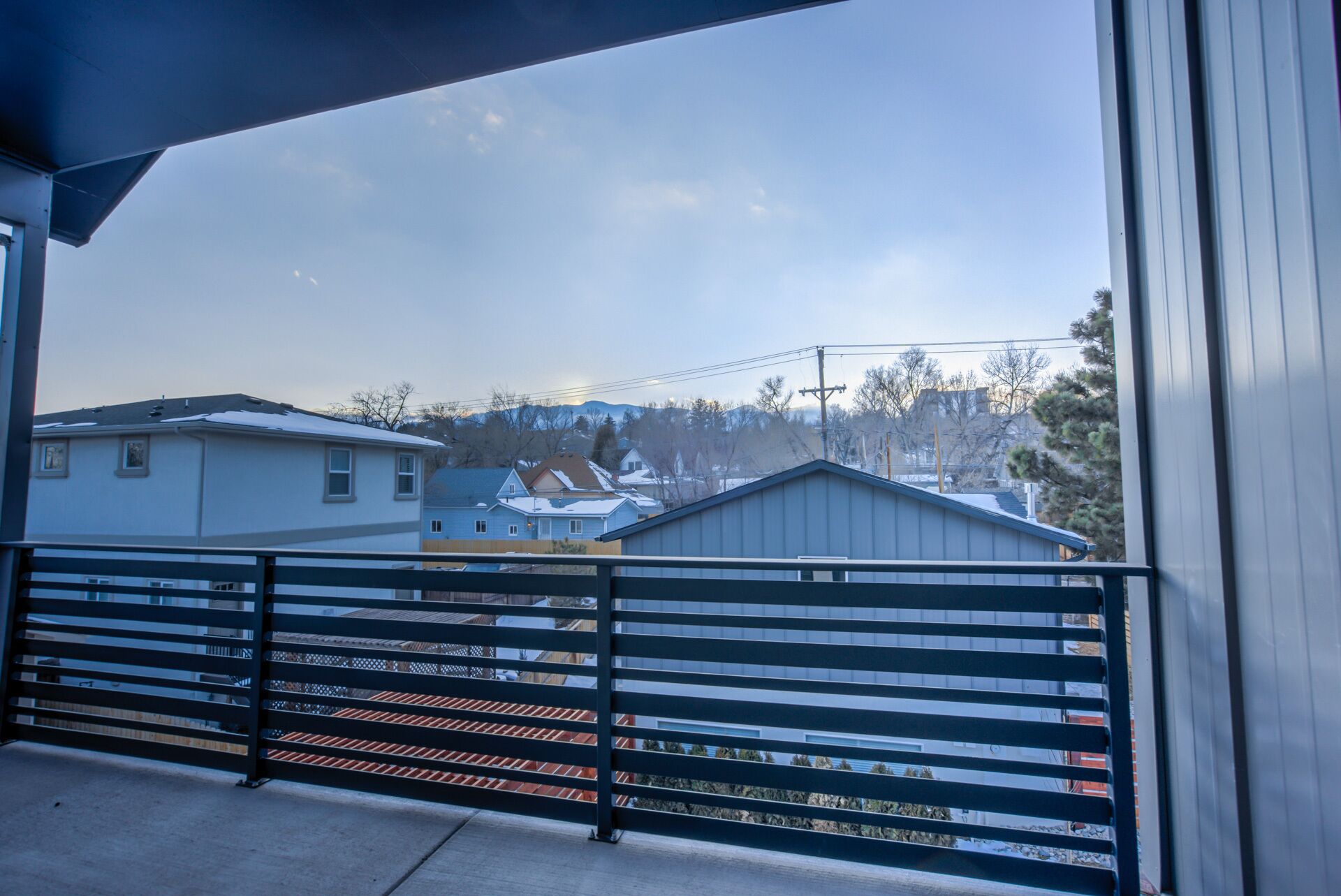 Een balkon met een metalen hekwerk met uitzicht op een woongebied met huizen en een berg op de achtergrond.