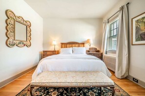 Une chambre à coucher bien aménagée, avec un grand lit, deux tables de chevet avec des lampes, un miroir décoratif, une fenêtre avec des rideaux et un tapis à motifs.