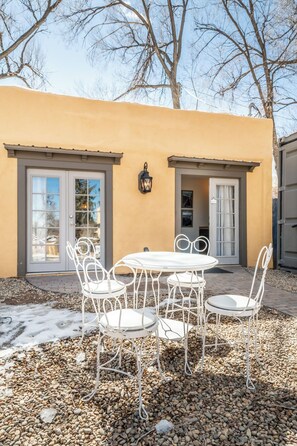 Une terrasse avec une table et des chaises, un bâtiment à la façade jaune et une porte avec une fenêtre.