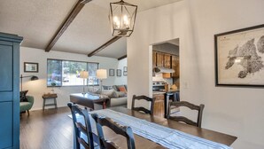Un coin repas avec une table et des chaises en bois, un lustre et une cuisine en arrière-plan.