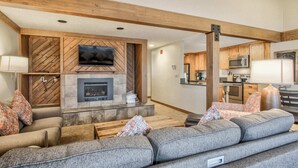 A modern living room with a fireplace, a flat-screen TV, and a kitchen in the background. - 3brbreckenridge Townhomebalcony Mtn Views Hot Tub (Breckenridge)