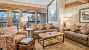 A cozy living room with a sofa, armchair, and coffee table, featuring large windows and a framed picture on the wall. - 3brbreckenridge Townhomebalcony Mtn Views Hot Tub (Breckenridge)
