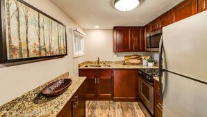 A compact kitchen with wooden cabinets, a granite countertop, a stainless steel refrigerator, and a painting on the wall. - 3BR Manitou Springs2min to Restaurants W/hot Tub! (Manitou Springs)