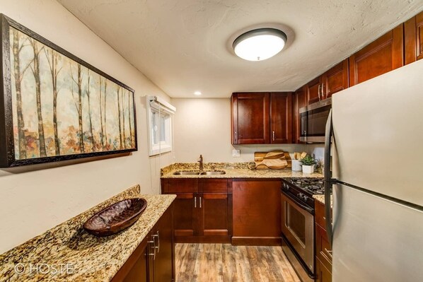 Una cocina compacta con armarios de madera, encimera de granito, refrigerador de acero inoxidable y un cuadro en la pared.
