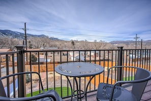 Een balkon met een ronde tafel en stoelen, met uitzicht op een woonwijk met huizen en bergen op de achtergrond.