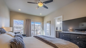 A hotel room with a bed, a ceiling fan, a large window with curtains, a dresser, and a TV. - 8BD Mnt Viewsgarden Of The Godslarge Groups (Colorado Springs)