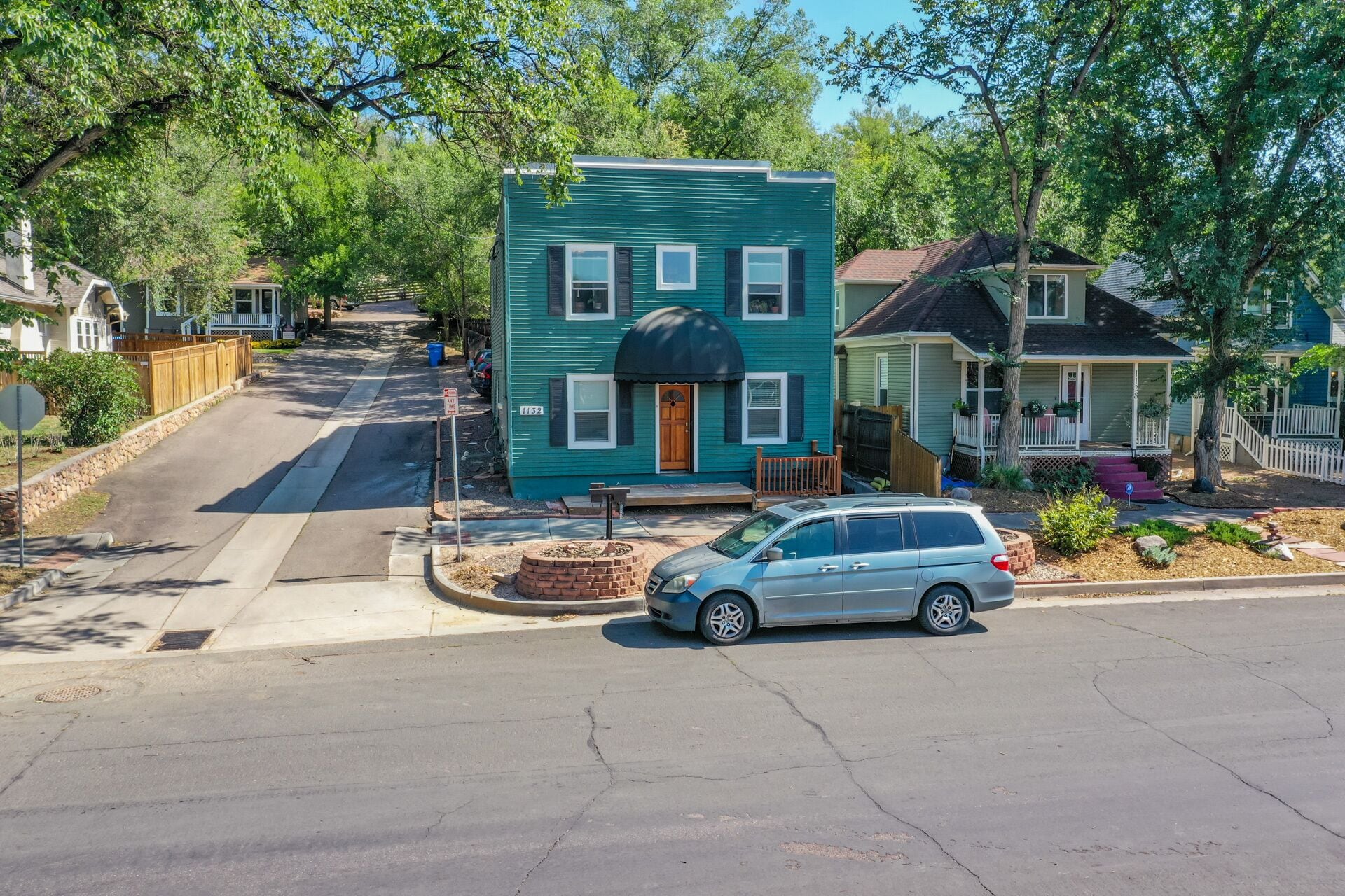 A two-story house with a dark green exterior, a front porch with a white railing, and a car parked in the driveway.