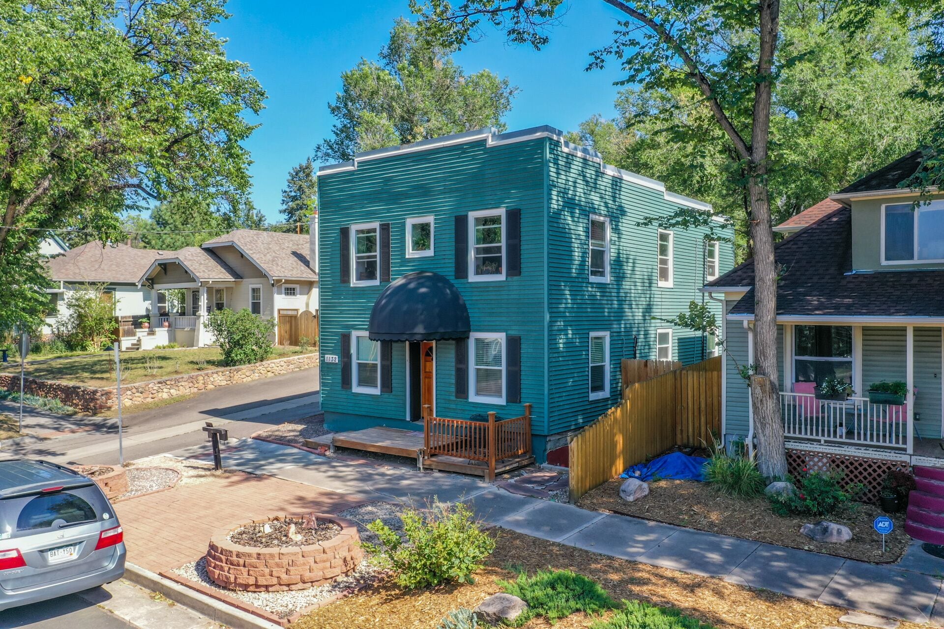A two-story house with a front porch, a small deck, and a brick fire pit in the yard.
