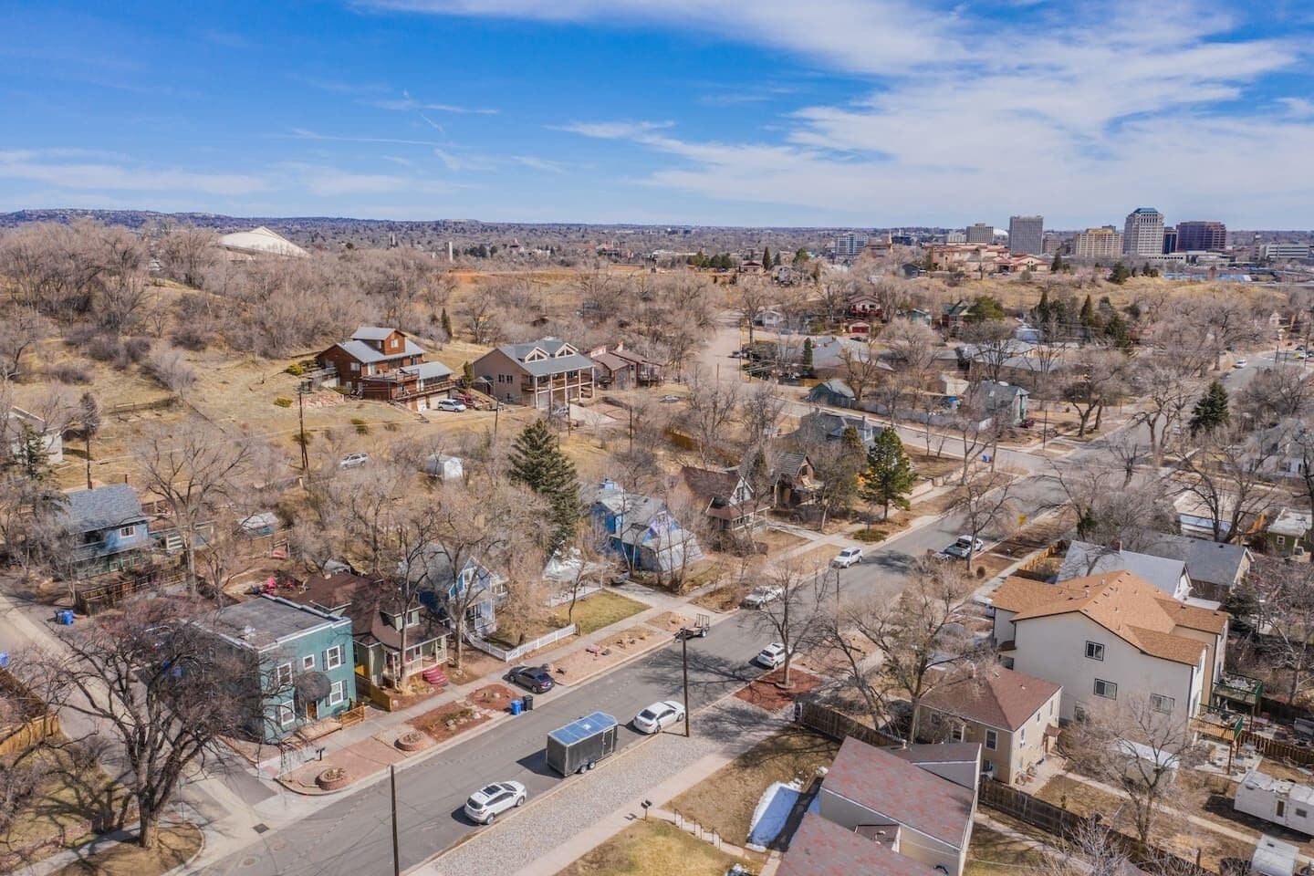 Vista aérea de una zona residencial con casas, calles y el perfil distante de una ciudad.