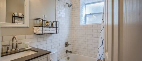 A bathroom with a toilet, sink, and bathtub. There is a window above the bathtub and a towel rack with towels.