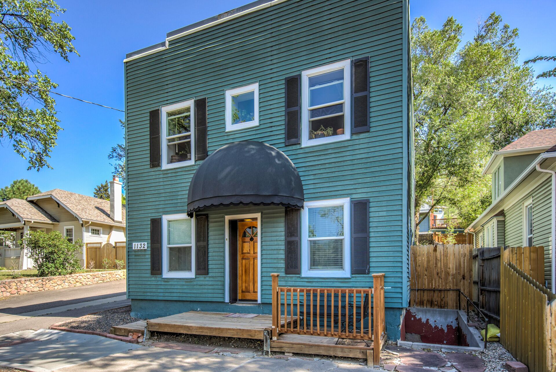 A two-story house with a dark green exterior, a front porch with a bench, and a black awning over the entrance.