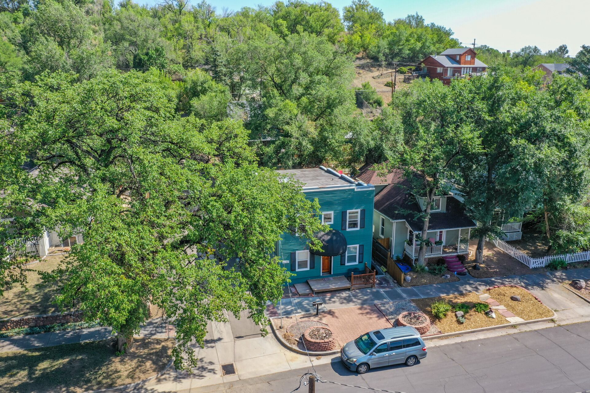 A residential area with a two-story house featuring a front porch, a driveway, and a parked car.