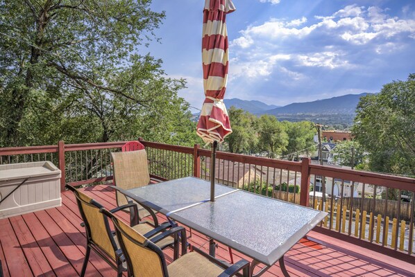 A deck with a table and chairs, an umbrella, and a view of mountains and trees. - 2brdowntown Occmountain Views & Grill (Colorado Springs)