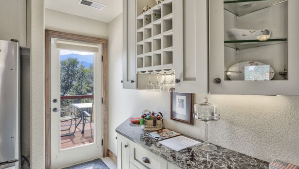 A kitchen with a marble countertop, a wine glass, and a basket of fruit. There is a door leading to a patio with a table and chairs. - 2brdowntown Occmountain Views & Grill (Colorado Springs)