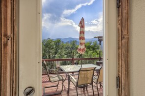 A deck with a table and chairs, a striped umbrella, and a view of trees and mountains. - 2brdowntown Occmountain Views & Grill (Colorado Springs)