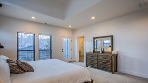 A bedroom with a large bed, a wooden dresser, a mirror, and a door leading to a bathroom. - 7brdowntown BIG & Moderngroups, Events & More! (Colorado Springs)