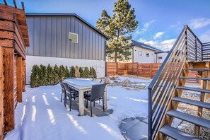 A snow-covered patio with a table and chairs, a wooden fence, and a building in the background. - 7brdowntown BIG & Moderngroups, Events & More! (Colorado Springs)