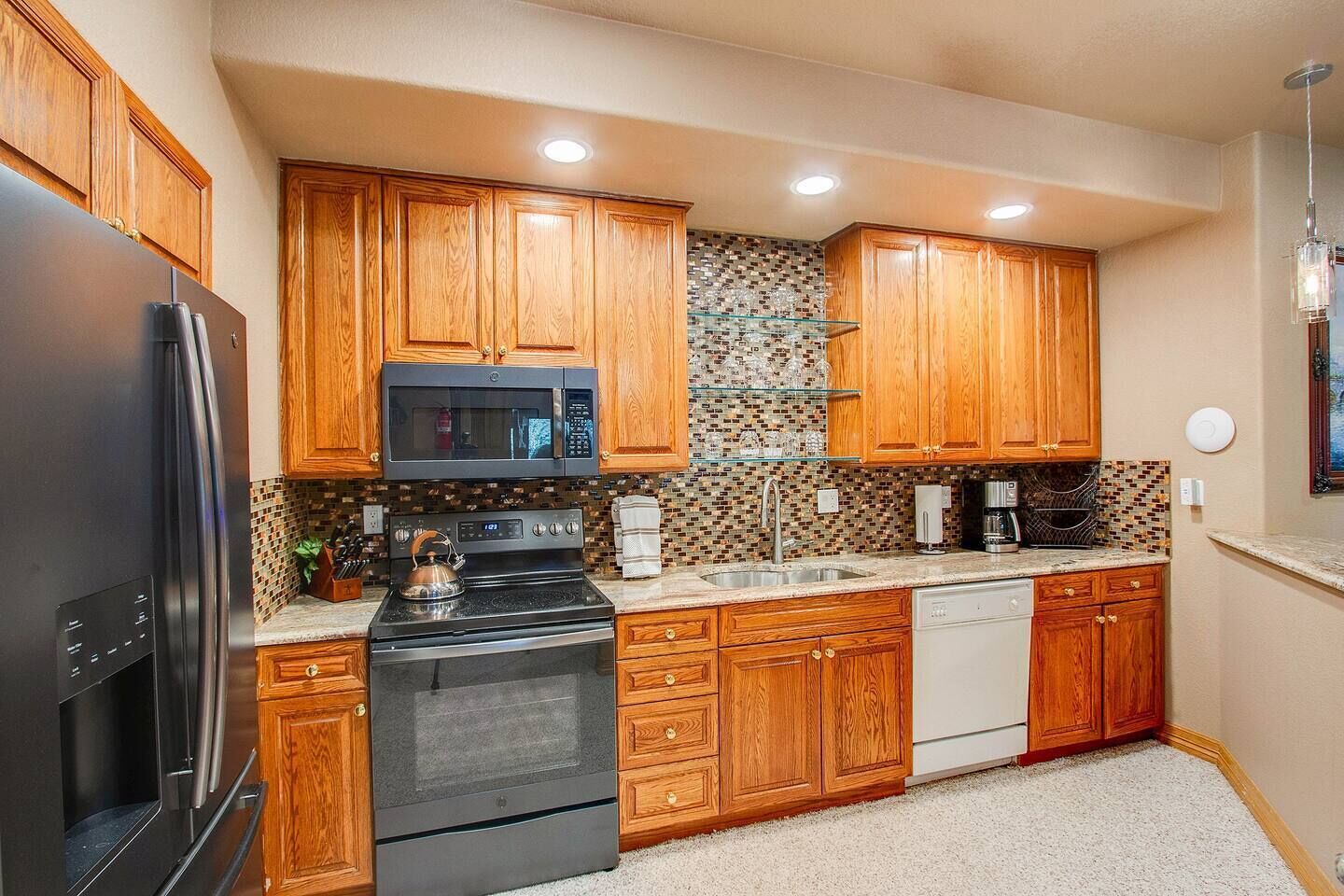 A kitchen with wooden cabinets, a stainless steel refrigerator, a microwave, a stove, and a coffee maker.