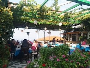 Un espace de restauration en plein air, avec des tables et des chaises, entouré de verdure et illuminé par des guirlandes lumineuses.