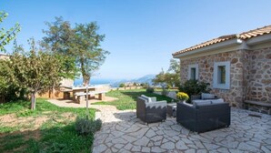 Un edificio de piedra con techo de tejas, zona de estar al aire libre con muebles de mimbre y vistas al paisaje.