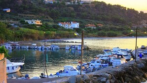 Un puerto deportivo con barcos amarrados, una costa rocosa y casas al fondo.