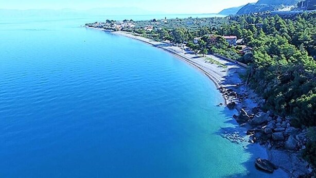 Una zona costera con mar azul cristalino, una playa estrecha y un litoral rocoso con vegetación.