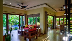 Un salón amplio con un sofá de madera, una zona de comedor con sillas y ventanas grandes que ofrecen vistas al exterior.