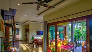 Amplia sala de estar con ventilador de techo, una mesa de comedor con un florero y vistas al exterior a través de puertas correderas grandes.