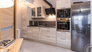 A modern kitchen with light wood cabinets, a stainless steel refrigerator, a microwave, and an oven. - Elegant Modern House in St Vaast la Hougue (Saint-Vaast-la-Hougue)
