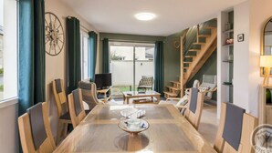 A dining area with a large wooden table, chairs, and a television. - Elegant Modern House in St Vaast la Hougue (Saint-Vaast-la-Hougue)
