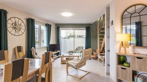 A modern living room with a dining area, a TV, and a staircase leading to an upper floor. - Elegant Modern House in St Vaast la Hougue (Saint-Vaast-la-Hougue)