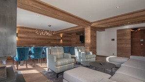 A modern living room with wooden paneling, blue chairs, and a grey sofa. - Ski-in/Ski-out Apartment with Panoramic Views and Luxury Amenities in Méribel (Méribel)