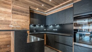 A modern kitchen with dark cabinetry, wooden accents, and built-in appliances. - Ski-in/Ski-out Apartment with Panoramic Views and Luxury Amenities in Méribel (Méribel)