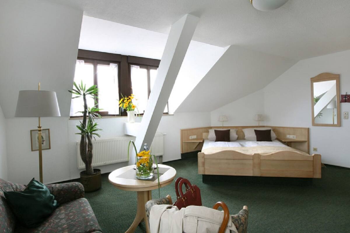 Een hotelkamer met een bed, een bank, een tafel met een bloevas, een lamp en een raam met uitzicht.