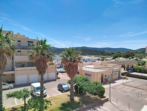 A coastal hotel with a parking lot, palm trees, and a view of the sea and mountains.