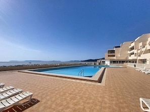 A rooftop pool with a clear view of the sea, surrounded by lounge chairs and a modern building.