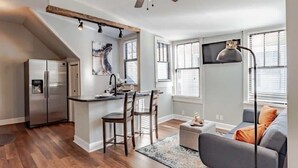 A modern kitchen with a central island, a dining area with chairs, a sofa, and a ceiling fan. - Mins from Downtown & Dining, Dauphin Darling 4 (Mobile)