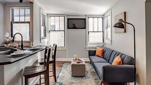A modern living room with a sofa, ottoman, and dining area with chairs and a table. - Mins from Downtown & Dining, Dauphin Darling 4 (Mobile)