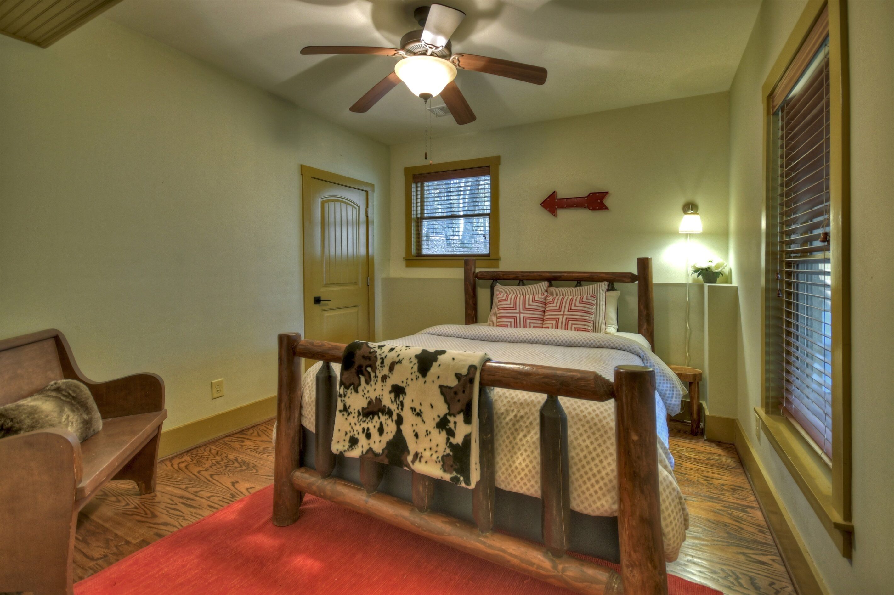 A bedroom with a bed, a wooden bench, a ceiling fan, a window, and a door.
