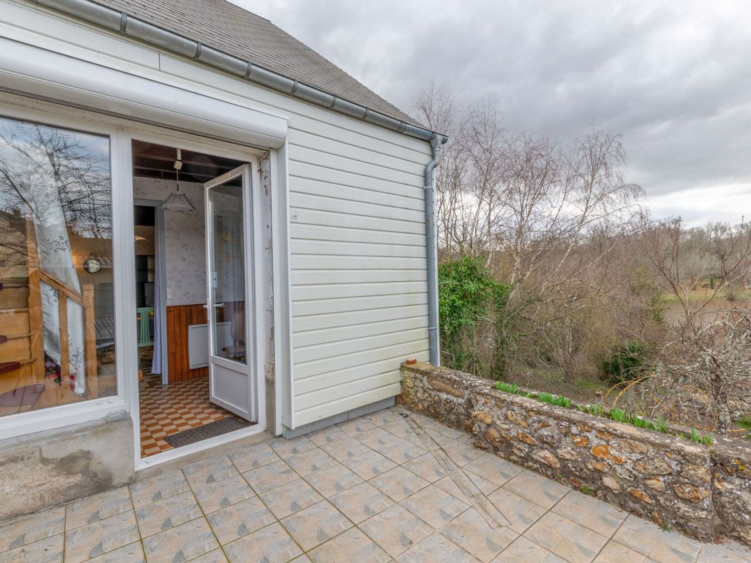 A house with a large glass door leading to a tiled patio area.