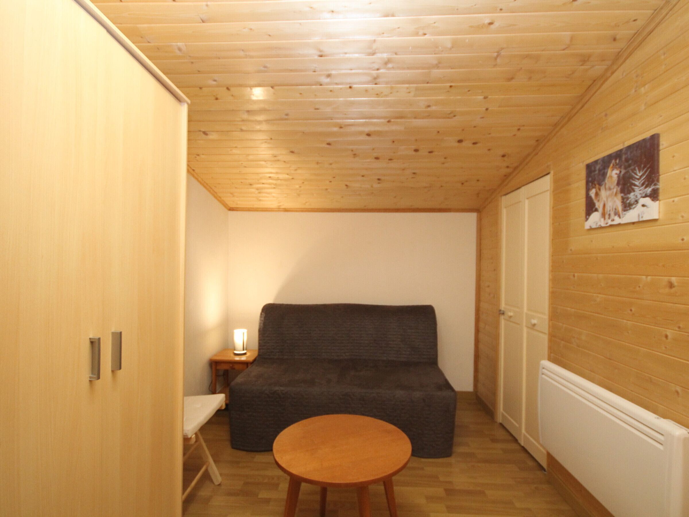 Une petite pièce accueillante avec un plafond en bois, un canapé gris, une petite table ronde et un radiateur blanc.