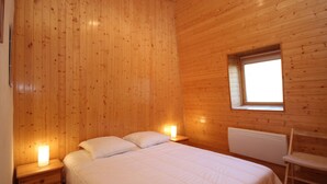 A wooden-paneled bedroom with a bed, bedside lamps, and a window. - Mont-Dore: 4BR Duplex with Balcony, Garage, and Wi-Fi (Mont-Dore)