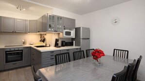 A modern kitchen with grey cabinets, a microwave, a refrigerator, and a dining table with chairs. - Mont-Dore: 4BR Duplex with Balcony, Garage, and Wi-Fi (Mont-Dore)