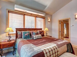 Een slaapkamer met een groot bed, twee nachtkastjes, een raam met zonwering en een deur die naar een andere kamer leidt.