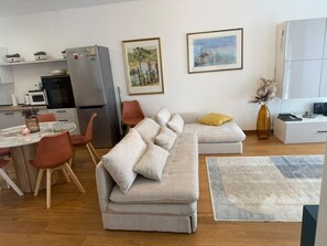 A modern living room with a grey sofa, a dining table with chairs, a kitchen area with appliances, and artwork on the walls. - Elizaveta apartment with lake view and terrace (Oggebbio)