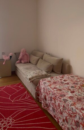 Ein Schlafzimmer mit einem Bett, einem Nachttisch, einer rosa Flamingo-Spielzeugfigur und einem roten Teppich mit Blumenmuster.