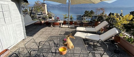 A patio with outdoor furniture, a large umbrella, and a view of a lake and mountains.